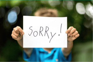 Child holding a handwritten sign on a white piece of paper that says, "Sorry!" in an effort to rebuild trust