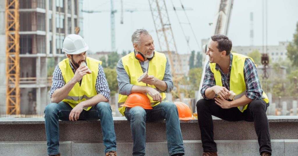 Three men wearing construction vests and hats talking
