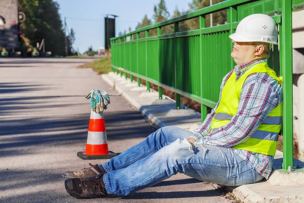 man wearing hard hat and safety vest resting against fence