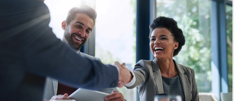 A man and a woman smiling. The woman is shaking another man's hand.