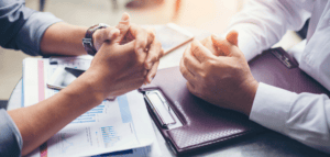 The hands and arms of two people sitting at a table negotiating